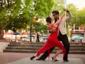 Para tańczy tango, latynoamerykański taniec towarzyski, w czerwonej sukni i eleganckim garniturze, na tle miejskiego placu.