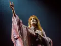 Florence Welch z Florence and the Machine na koncercie, w błyszczącej sukni, z uniesioną ręką.