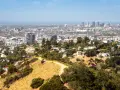 Widok na Los Angeles, miasto śmierci, z wzgórz porośniętych suchą trawą i drzewami. W oddali widać drapacze chmur.