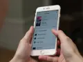 Ręce trzymają iPhone'a z otwartą aplikacją Apple Music. Widoczna lista utworów, która może pomóc w nauce, jak pobrać muzykę na iPhone'a.