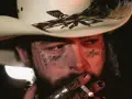 Post Malone w kapeluszu kowbojskim, z tatuażami na twarzy, pali papierosa. Jeden z najsłynniejszych wykonawców muzyki country.