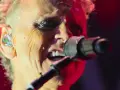 Dave Gahan z Depeche Mode śpiewa, a jego twarz oświetlają czerwone światła. Słuchawka w uchu błyszczy, gdy wykonuje swoje kultowe utwory.