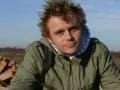 Piotr Rogucki, w otoczeniu gruzu, z charakterystyczną fryzurą, jakby inspirowany swoimi utworami.