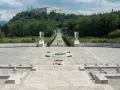 Cmentarz żołnierzy na wzgórzu, z widocznym klasztorem na szczycie. Droga prowadzi do niego przez monumentalny plac z krzyżami i pomnikiem. To miejsce pamięci o bitwie pod **Cassino - trzeci / rzeka**.