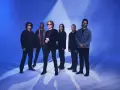 Zespół Simply Red gotowy na koncert w Polsce. Sześciu muzyków pozuje na tle niebieskiego światła.