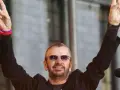 Ringo Starr z The Beatles pozdrawia fanów, unosząc ręce w geście pokoju.
