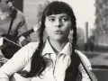 Młoda Karin Stanek z warkoczami śpiewa, grając na gitarze. W tle zespół muzyczny.
