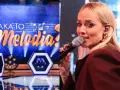 Ola Radwan śpiewa w programie "Jaka to melodia?". Na scenie widać neonowe dekoracje i logo programu.
