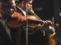 Skrzypek grający melodię, która mogłaby być jedną z piosenek o Krakowie. W tle inni muzycy orkiestry.