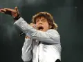 Mick Jagger, wokalista zespołu, śpiewa z mikrofonem, gestykulując ręką.