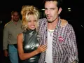 Pamela Anderson i Tommy Lee, ikony lat 90., pozują do zdjęć. Pamela w błyszczącej sukience, Tommy w kratowanej koszuli.