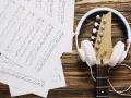 Nuty i gitara z białymi słuchawkami. Idealne do tego, by znaleźć piosenkę po nuceniu i stworzyć własną melodię.