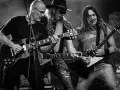 Trzech gitarzystów grających na scenie, przypominających klimatem ballady rockowe lat 80.