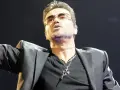 George Michael w okularach, w czarnej marynarce i z naszyjnikiem, śpiewający swoje niezapomniane utwory.