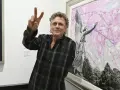 Rick Allen, perkusista Def Leppard, pozuje z uniesionym znakiem pokoju obok obrazu z aniołem i kwitnącymi drzewami.