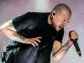 Chester Bennington z Linkin Park, z tatuażami na ramionach, śpiewa do mikrofonu z pasją.