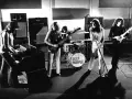 Zespół Deep Purple w akcji. Muzycy grają na instrumentach, w tle perkusja z logo zespołu.