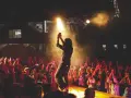Artysta na scenie podczas koncertu plenerowego, tłum wiwatuje. Energia i emocje w powietrzu.