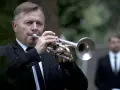 Mężczyzna w garniturze gra na trąbce. To jego ulubiona piosenka na pogrzebie, która wzrusza zgromadzonych.