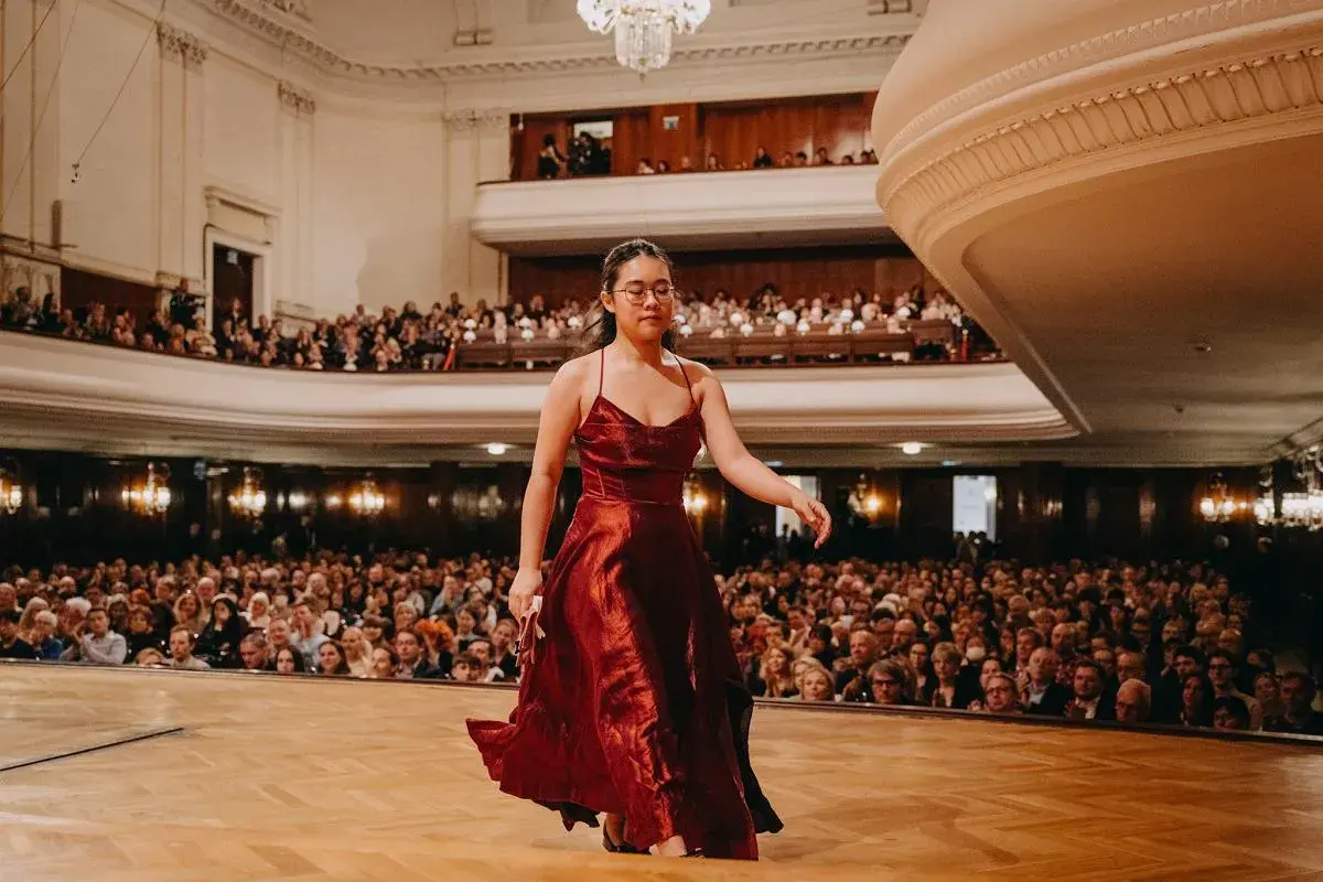 Młoda pianistka w czerwonej sukni wchodzi na scenę, by wykonać nokturn. Publiczność w teatrze czeka na występ.