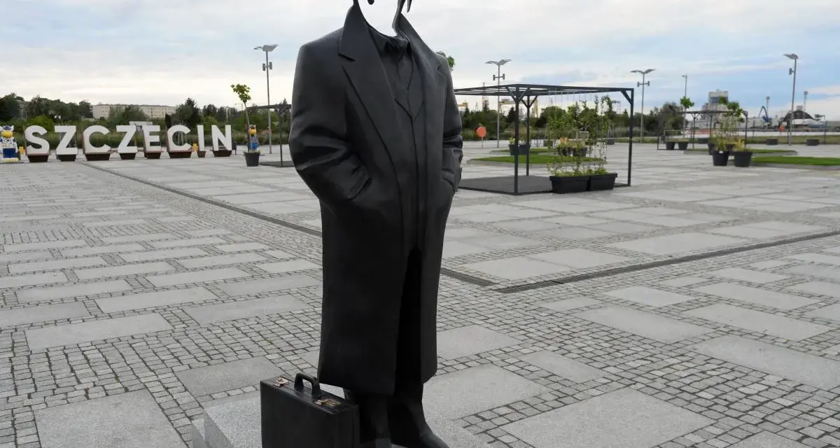 Pomnik Krzysztofa Jarzyny w Szczecinie, z charakterystyczną teczką u stóp, stoi na placu z napisem "SZCZECIN" w tle.