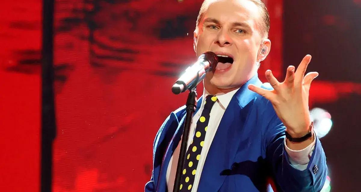 Artysta w niebieskiej marynarce i krawacie w grochy śpiewa do mikrofonu. To jego piosenka do góry, pełna energii.