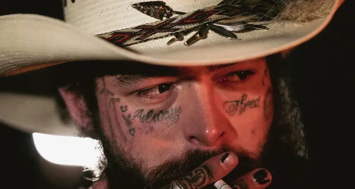 Post Malone w kapeluszu kowbojskim, z tatuażami na twarzy, pali papierosa. Jeden z najsłynniejszych wykonawców muzyki country.