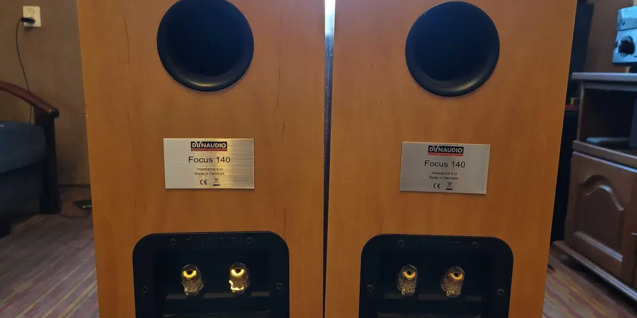Dwa głośniki Dynaudio Focus 140 w drewnianej obudowie, z widocznymi złączami i tabliczkami znamionowymi.