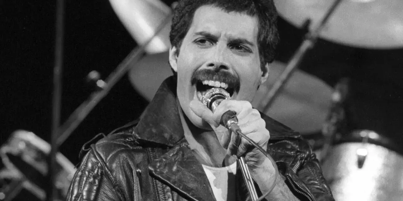 Freddie Mercury przed śmiercią, w skórzanej kurtce, śpiewa do mikrofonu. W tle widać perkusję.