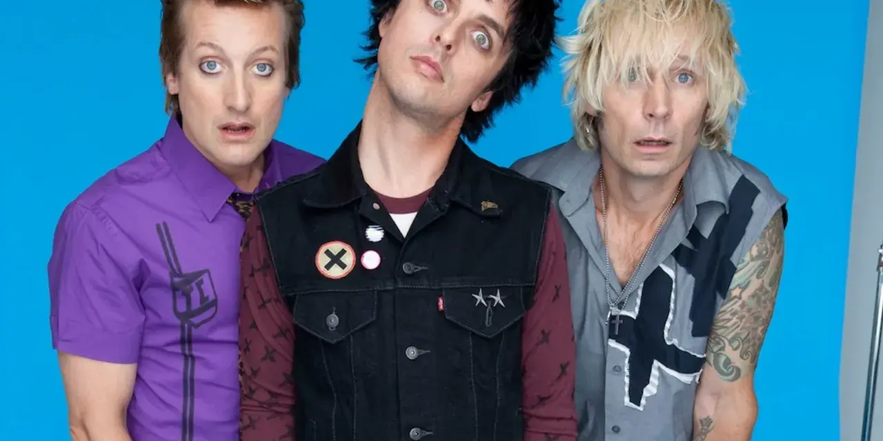 Trzech członków zespołu Green Day Polska z wyrazistymi minami na niebieskim tle.