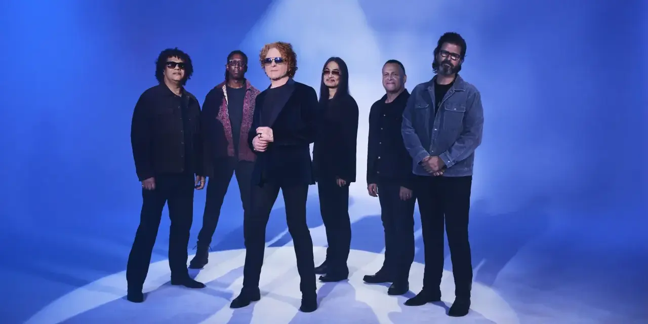 Zespół Simply Red gotowy na koncert w Polsce. Sześciu muzyków pozuje na tle niebieskiego światła.