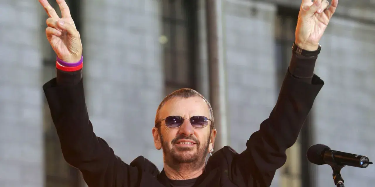 Ringo Starr z The Beatles pozdrawia fanów, unosząc ręce w geście pokoju.
