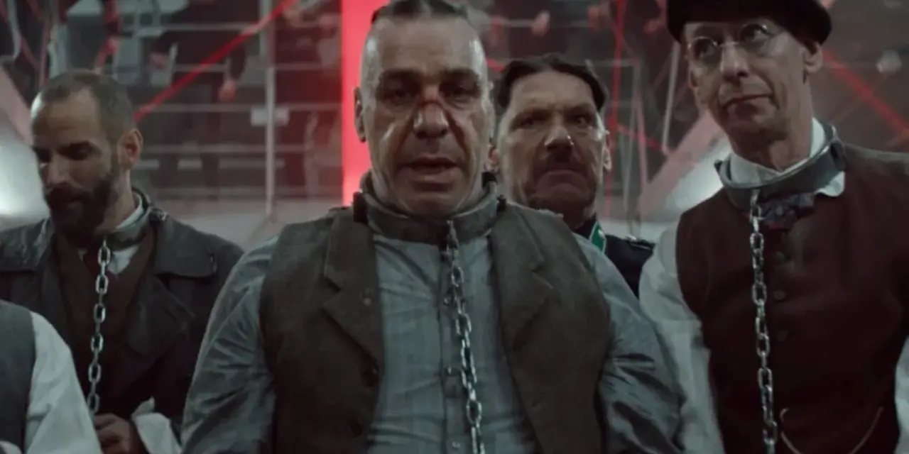 Rammstein - Deutschland: mężczyźni w łańcuchach, w tle czerwone światła i ludzie na schodach.