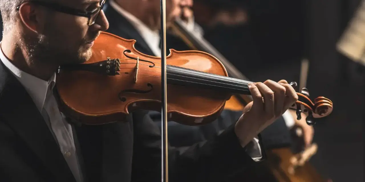 Skrzypek grający melodię, która mogłaby być jedną z piosenek o Krakowie. W tle inni muzycy orkiestry.