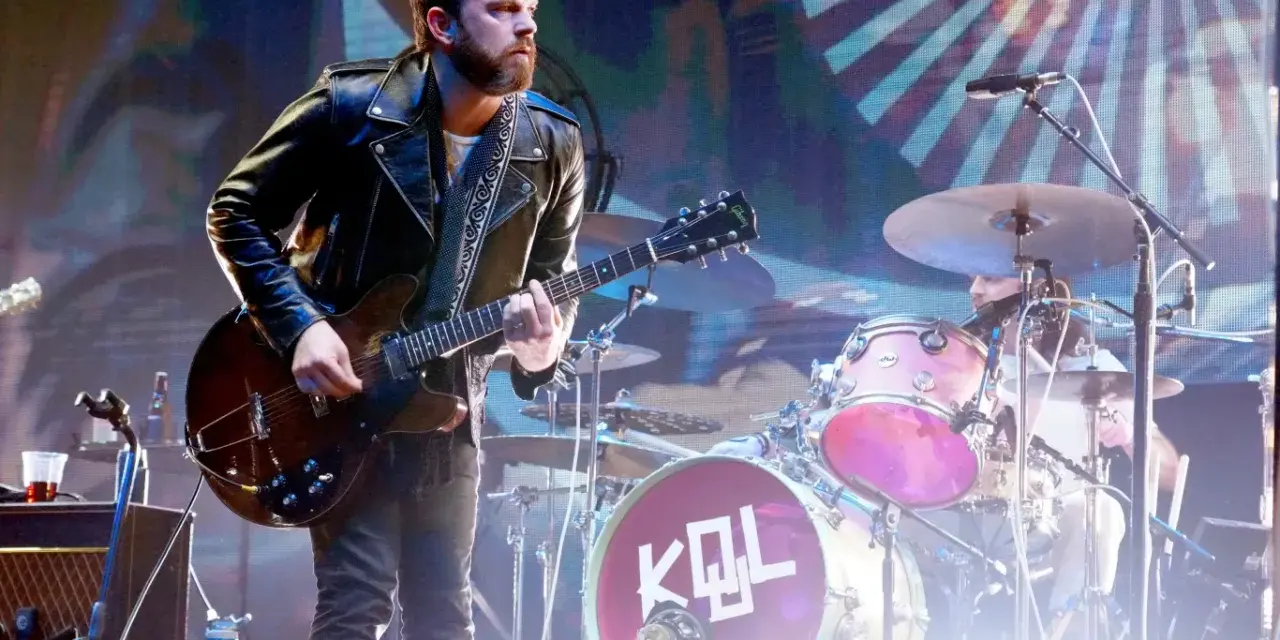 Gitarzysta Kings of Leon Polska w skórzanej kurtce gra na scenie. W tle perkusja z logo KQL.