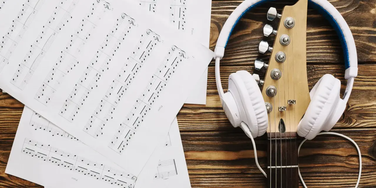 Nuty i gitara z białymi słuchawkami. Idealne do tego, by znaleźć piosenkę po nuceniu i stworzyć własną melodię.
