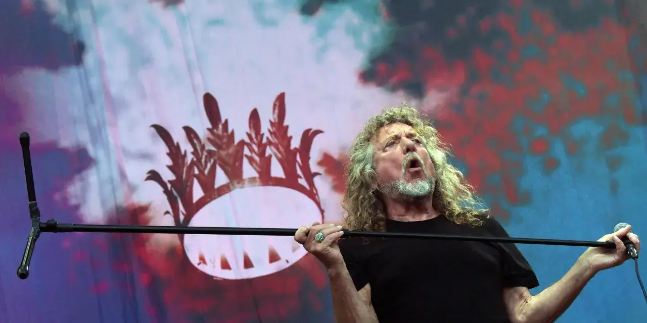 Wokalista Led Zeppelin, Robert Plant, śpiewa z pasją na tle scenografii z koroną.