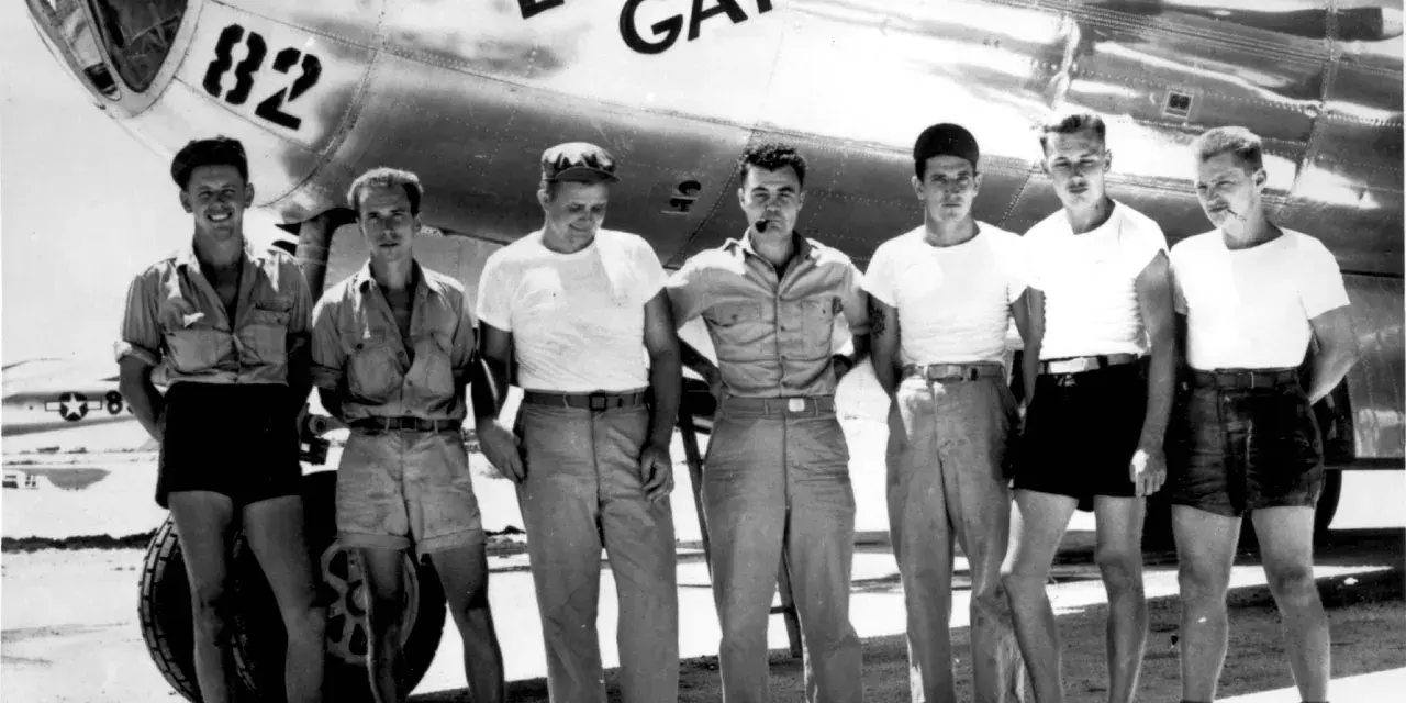 Siedmiu mężczyzn pozuje przed samolotem B-29 o nazwie "Enola Gay".
