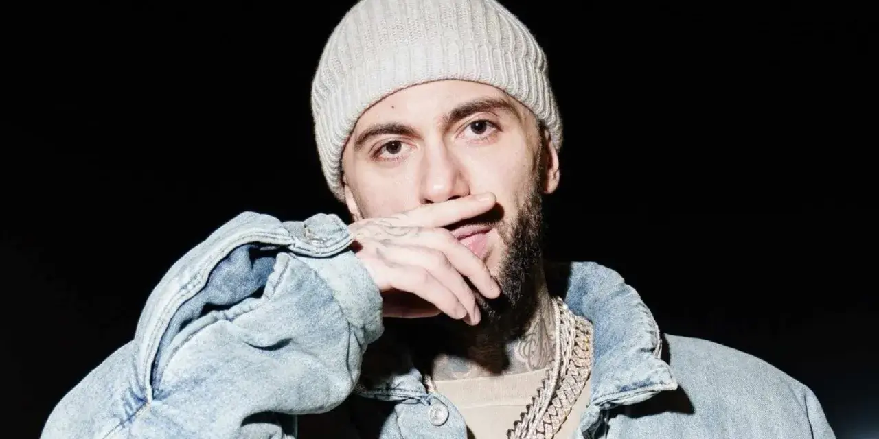 Malik Montana w czapce i jeansowej kurtce, z dłonią na ustach, gotowy na koncert.