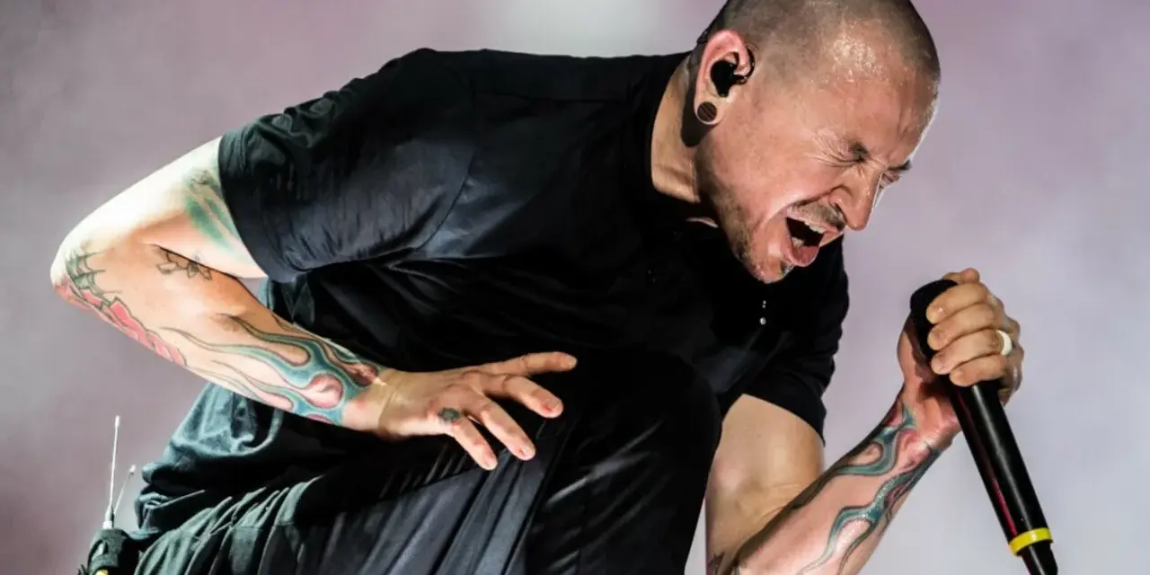 Chester Bennington z Linkin Park, z tatuażami na ramionach, śpiewa do mikrofonu z pasją.