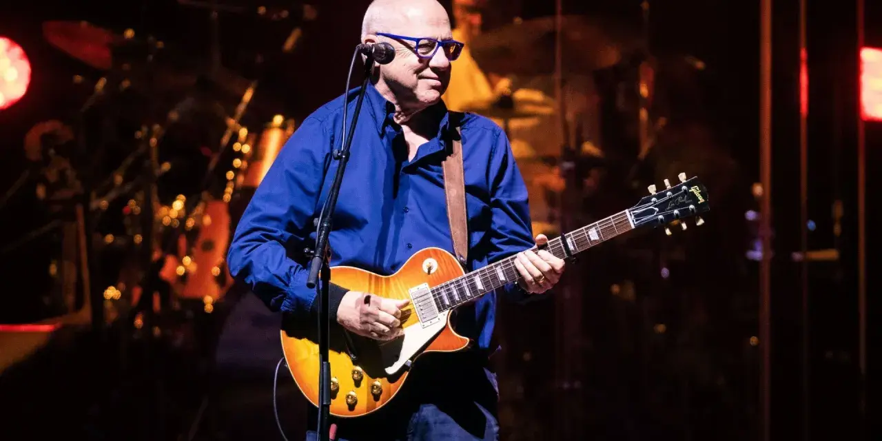 Mark Knopfler na scenie, grając na gitarze Gibson Les Paul. Jego charakterystyczne utwory brzmią w tej chwili na żywo.