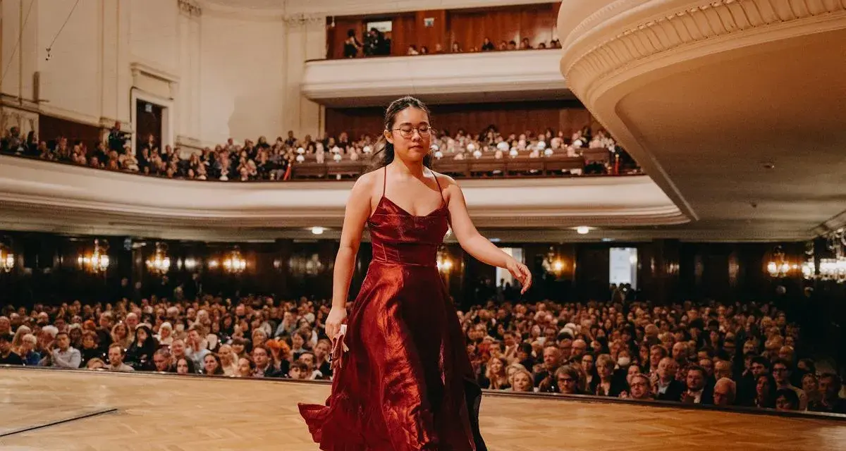 Młoda pianistka w czerwonej sukni wchodzi na scenę, by wykonać nokturn. Publiczność w teatrze czeka na występ.