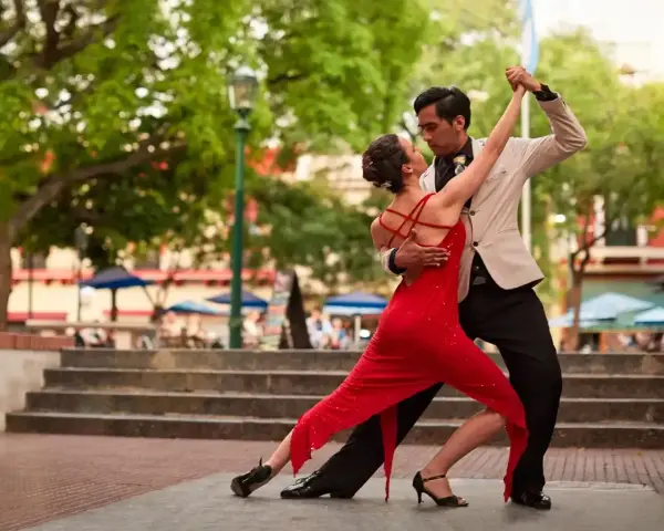 Para tańczy tango, latynoamerykański taniec towarzyski, w czerwonej sukni i eleganckim garniturze, na tle miejskiego placu.