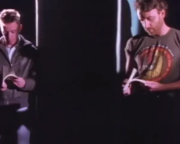 Dwóch mężczyzn czyta. Jeden w kurtce, drugi w koszulce z napisem. Atmosfera jak z "Blue Monday" New Order.
