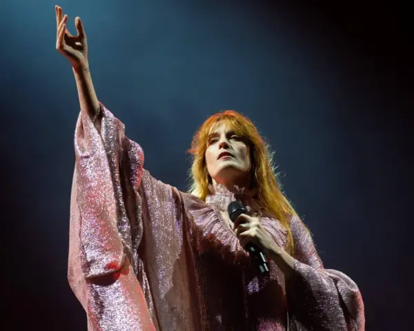 Florence Welch z Florence and the Machine na koncercie, w błyszczącej sukni, z uniesioną ręką.