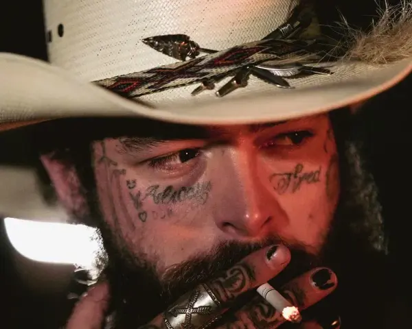 Post Malone w kapeluszu kowbojskim, z tatuażami na twarzy, pali papierosa. Jeden z najsłynniejszych wykonawców muzyki country.