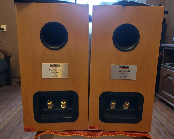 Dwa głośniki Dynaudio Focus 140 w drewnianej obudowie, z widocznymi złączami i tabliczkami znamionowymi.