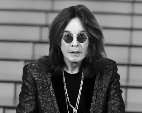 Ozzy Osbourne w okularach i błyszczącej marynarce, z naszyjnikami. Plotki o tym, że Ozzy Osbourne nie żyje, są fałszywe.