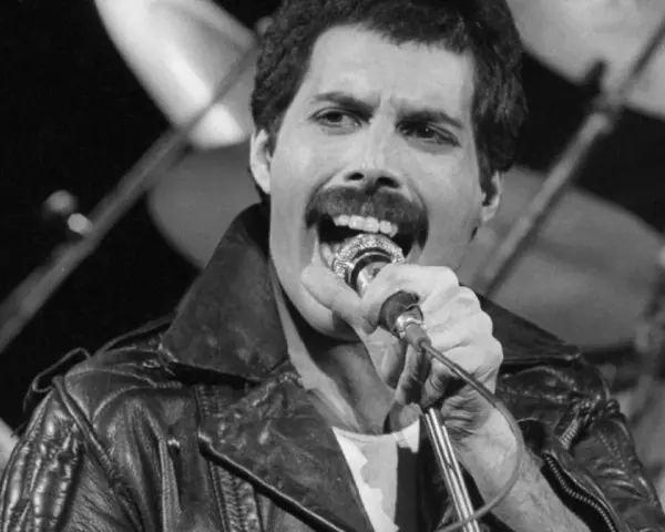 Freddie Mercury przed śmiercią, w skórzanej kurtce, śpiewa do mikrofonu. W tle widać perkusję.
