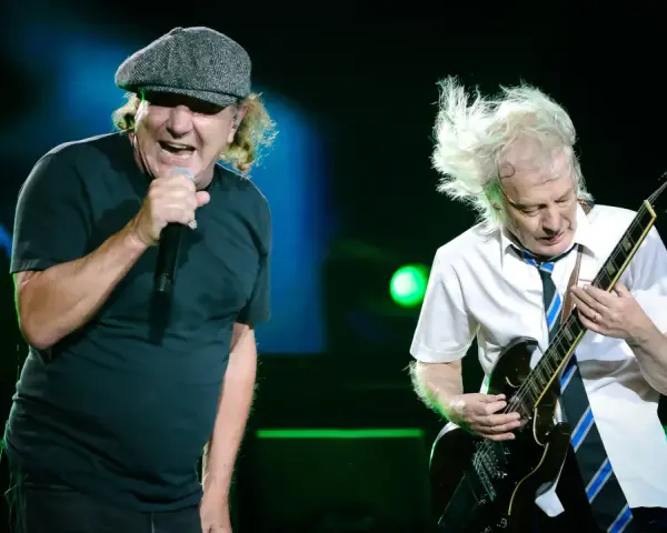 Brian Johnson śpiewa, Angus Young gra na gitarze podczas jednego z legendarnych **AC/DC koncertów**.